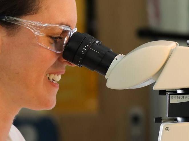 Woman with safety goggles looking through a biology microscope