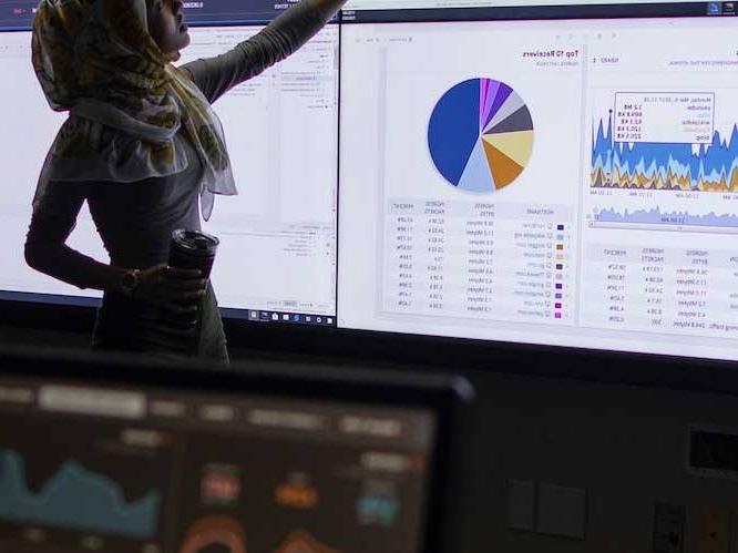 Woman standing infront of projectors pointing to graphs on the screen